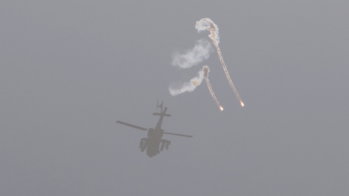 A helicopter with missiles and artillery casts a shadow on a beach as it hurtles towards Gaza