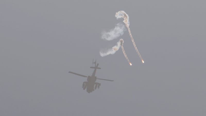 A helicopter with missiles and artillery casts a shadow on a beach as it hurtles towards Gaza