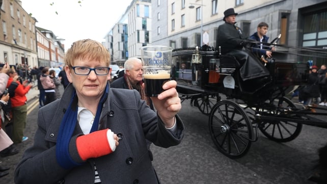 A woman holds up a pint of Guinness on Pearse Street as the funeral procession makes its way through the streets of Dublin