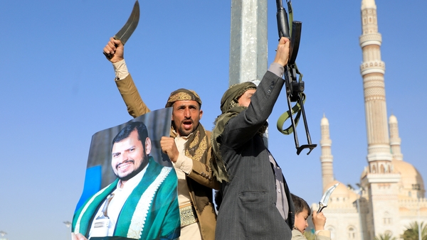 Houthi fighters, one holding a portrait of Huthi leader Abdul Malik al-Houthi, brandish their weapons during a protest following US and British strikes on Yemen