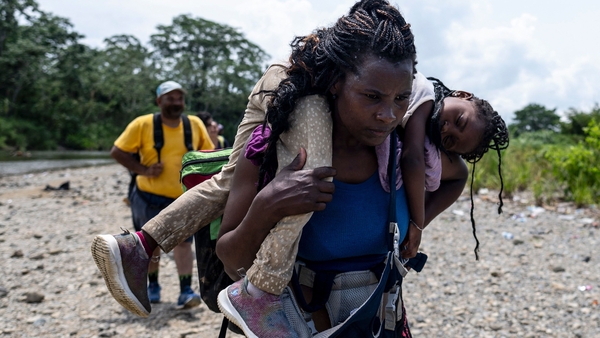 A migrant woman walks by the jungle carrying her daughter in Darien Province in Panama