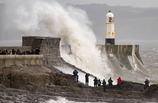 Onlookers watch waves crash against the harbour wall in Porthcawl, Wales