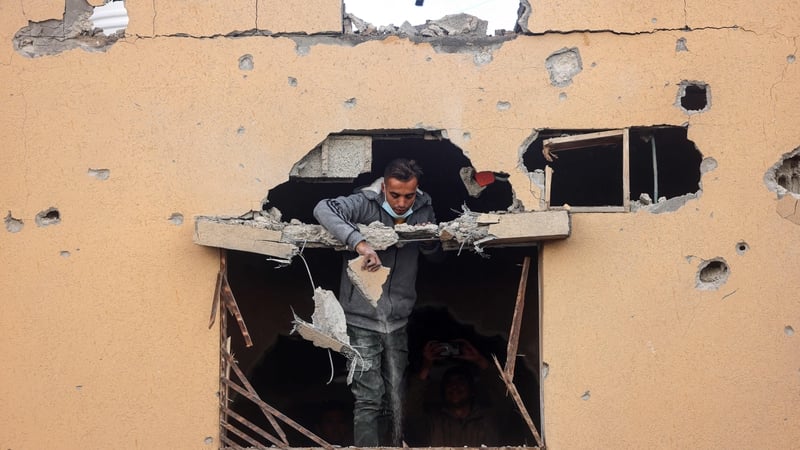 A man looks through the window of a building damaged by Israeli bombing, shows members of a family standing on a rooftop, in Rafah in south Gaza