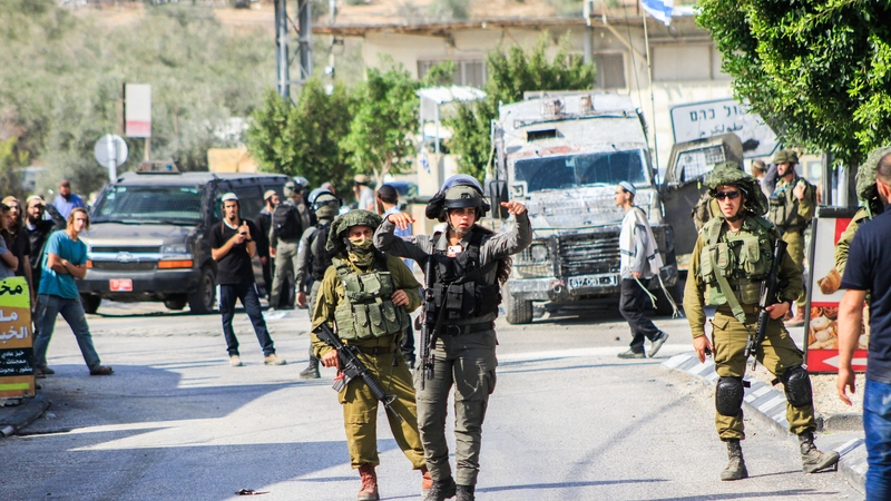 Israeli soldiers protecting Jewish settlers who launched an attack on the Palestinian town of Deir Sharaf following a shooting that killed an Israeli