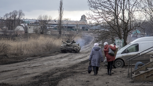 Civilians walk on a road as a tank drives by in a village nearby Avdiivka frontline
