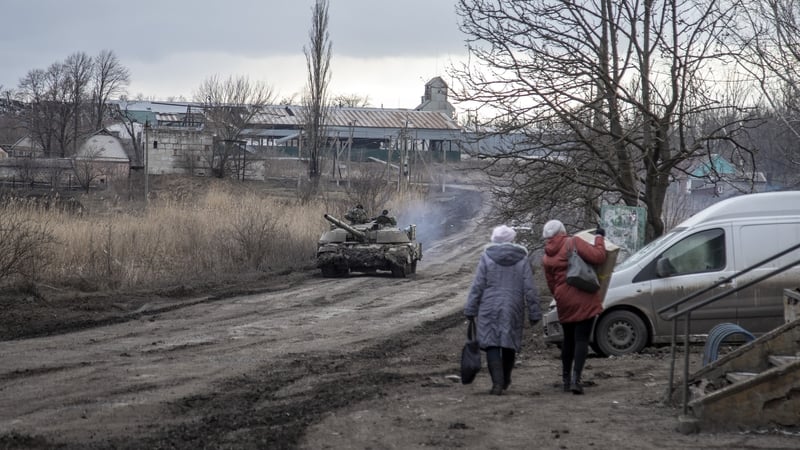 Civilians walk on a road as a tank drives by in a village nearby Avdiivka frontline