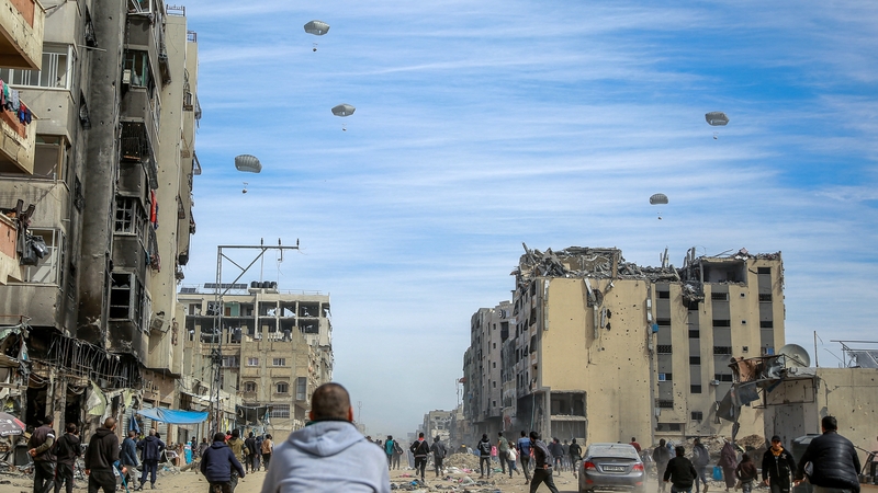 Palestinians run along a street as aid is airdropped in Gaza