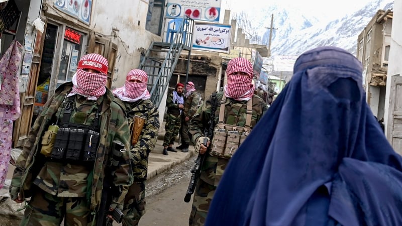 Taliban security personnel stand guard as an Afghan burqa-clad woman walks along a street at a market in the Baharak district of Badakhshan province (Photo by Wakil KOHSAR / AFP)