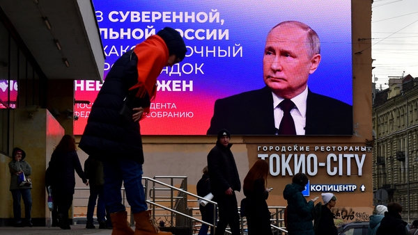 People are seen in front of a digital screen displaying Vladimir Putin and a quote from his recent address in Saint Petersburg