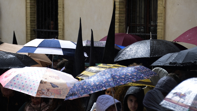 Penitents from the 'San Bernardo' brotherhood walk along the street as bystanders shelter under umbrellas