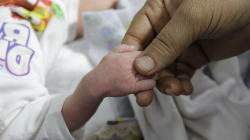 A man holds a hand of a baby, hospitalized due to malnutrition and dehydration, at Kamal Adwan Hospital in Beit Lahia, Gaza
