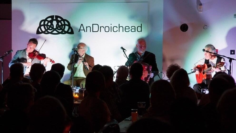 Ceoltóirí agus crabhd bailithe isteach sa Droichead ar Bhóthar Chúic