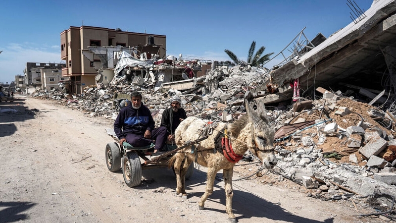Two men sit in a donkey-drawn cart moving past the rubble of a destroyed building in Khan Yunis, Gaza