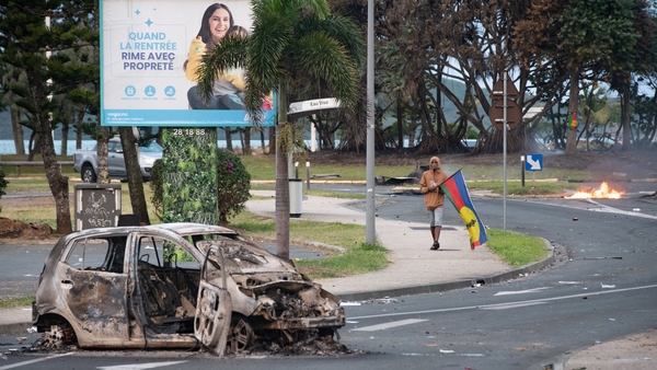 A man walks past a burnt out car carrying a flag of the Socialist Kanak National Liberation Front (FLNKS)