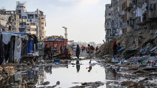Palestinians walk around a puddle in front of destroyed buildings and tents in Khan Younis in southern Gaza