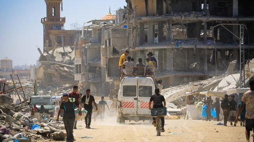 Displaced people walk along a devastated street in Khan Yunis