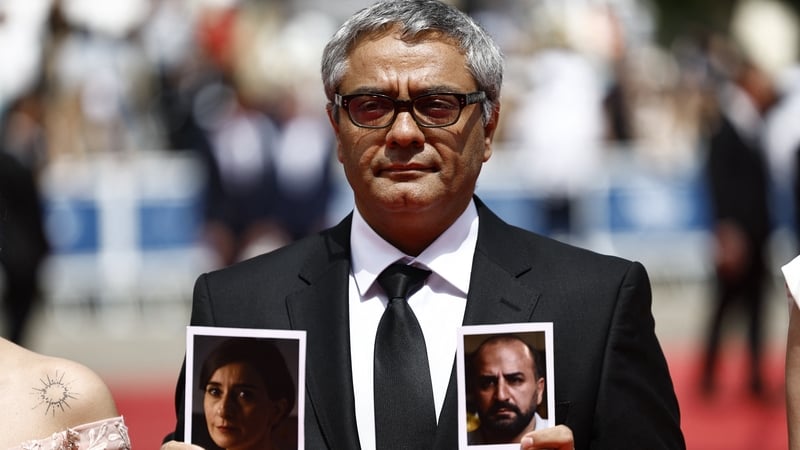 Iranian director Mohammad Rasoulof holds portraits of Iranian actors Missagh Zareh (right) and Soheila Golestani (left) as he arrives for the premiere of The Seed of the Sacred Fig at the Cannes Film Festival