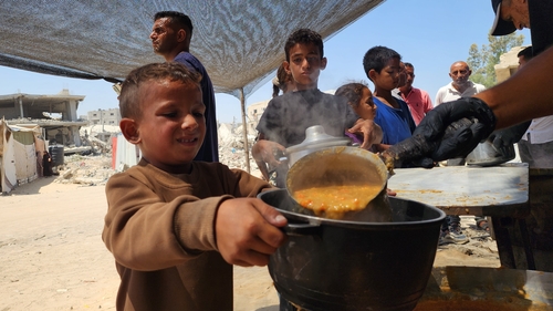 Displaced Palestinians, including children, wait in queues for food