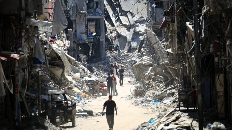 Palestinian men walk along a narrow street past destroyed buildings in Khan Yunis