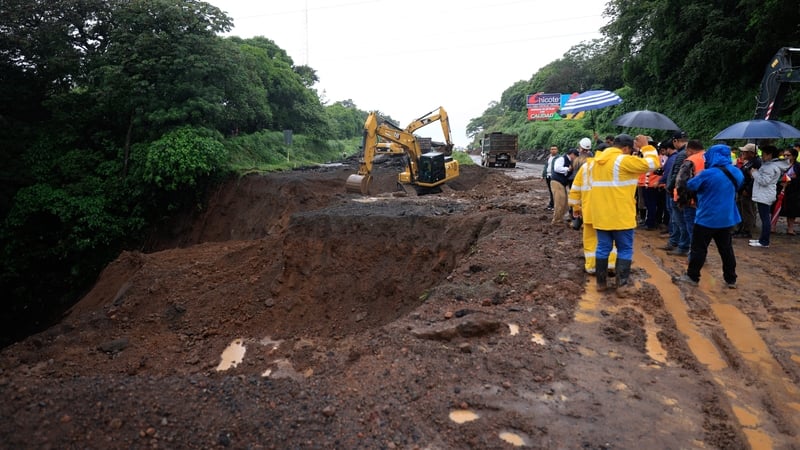 Heavy machinery and emergency personnel work at the scene of the collapse of a drainage underneath a road due to the heavy rains