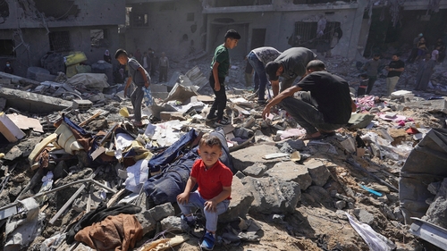 A Palestinian boy sits as people search the rubble of a family home destroyed in by Israeli bombing in al-Bureij refugee camp in Gaza