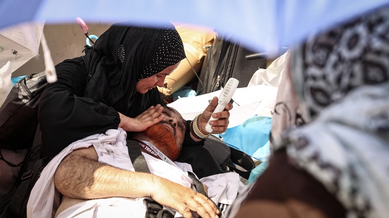 A woman uses a handheld fan to help cool down a man affected by the heat during the hajj pilgrimage