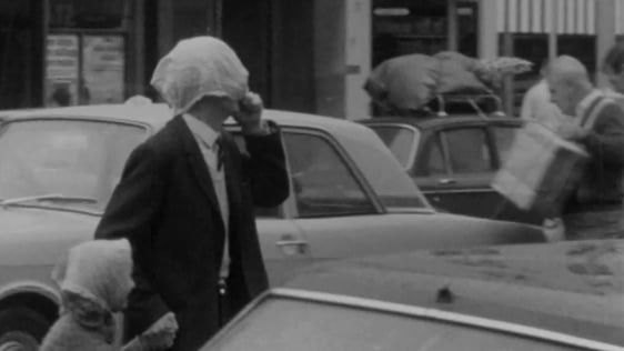 A man and his daughter use their handkerchiefs as headgear to fend off rain in Cork, 1969.