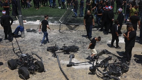 Members of the Druze community look at the damaged fence and scattered objects at the football pitch following the strike