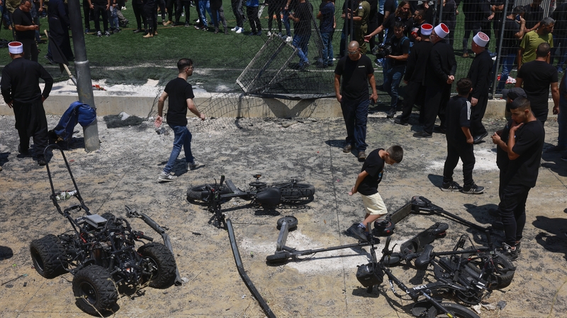 Members of the Druze community look at the damaged fence and scattered objects at the football pitch following the strike