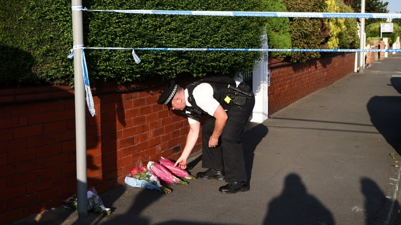A police officer lays floral tributes brought by well wishers on Hart Street in Southport, northwest England