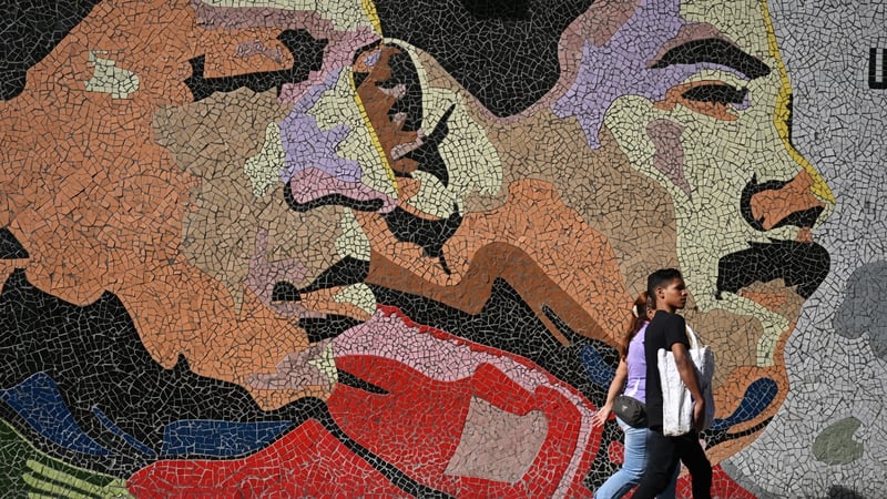 People walk past a mural of the late president Hugo Chavez and current President Nicolas Maduro in Caracas