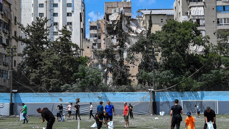 Residents clear the rubble in a football field facing the building that was hit a day earlier in an Israeli strike in Beirut's southern suburbs
