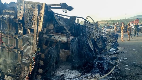Security personnel stand near the charred remains of vehicles which were attacked by separatist militants