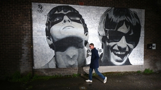 An Oasis fan is photographed next to a new mural depicting Liam and Noel Gallagher of Oasis