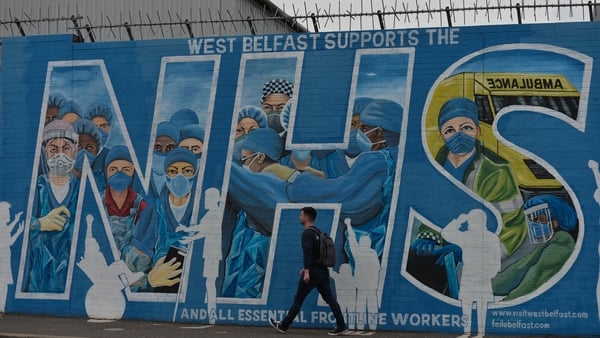 A man pictured walking past a mural reading showing support to NHS workers in the West Belfast area