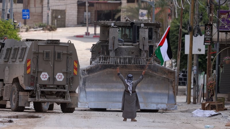 A Palestinian activist lifts a national flag towards an Israeli armoured vehicle and a bulldozer during a raid in Tulkarem this week