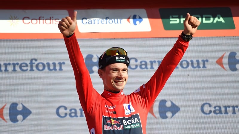 Primoz Roglic celebrates on the podium wearing the overall leader red jersey