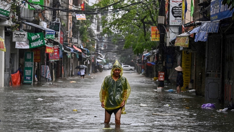 A man wearing a plastic poncho wades through flood waters on a street in Hanoi