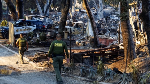 Riverside County Sheriff deputies walk past destroyed vintage cars next to a burned home off Ortega Highway in Lake Elsinore, California
