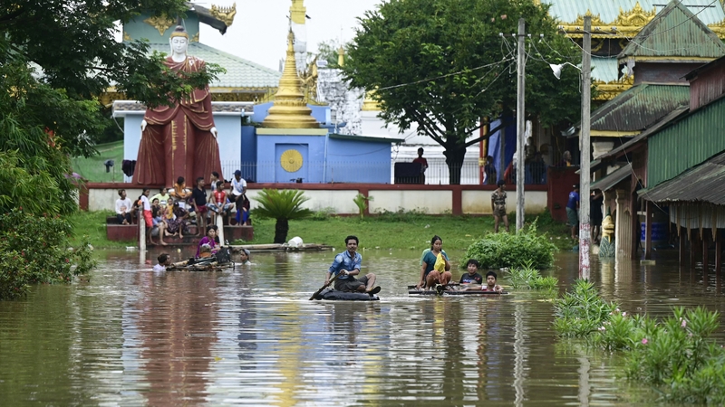 Flood-affected residents ride bamboo rafts while others gather on higher ground by a temple