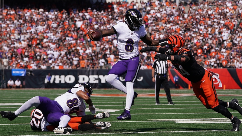 Lamar Jackson #8 runs the ball as Sam Hubbard of the Bengals attempts to make a tackle