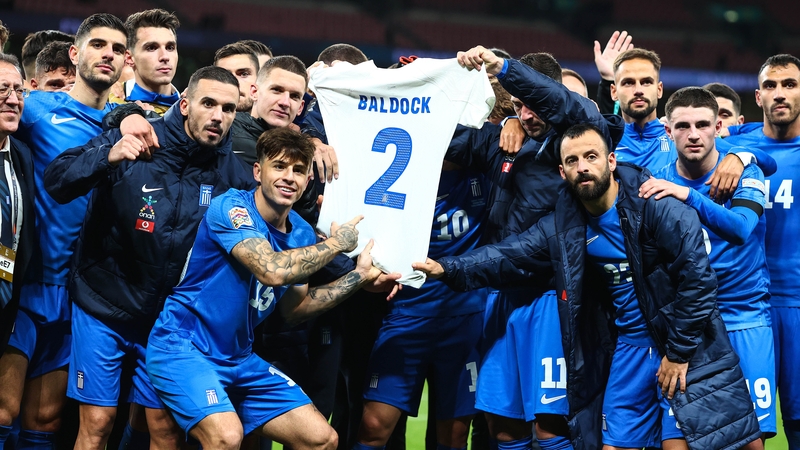 Greece players hold up a shirt bearing George Baldock's name and number after their victory over England
