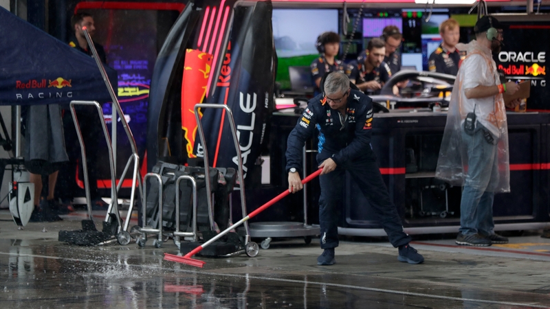 A Red Bull Racing team member sweeps rainwater