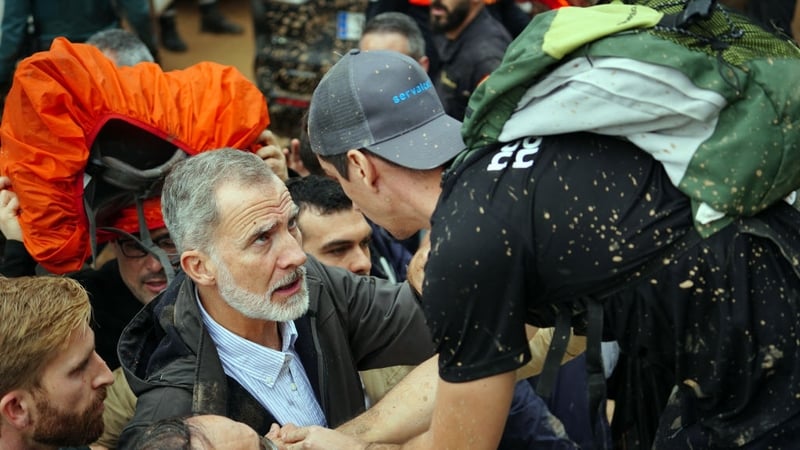 King Felipe VI of Spain (L) talks with a person as angry residents heckle him