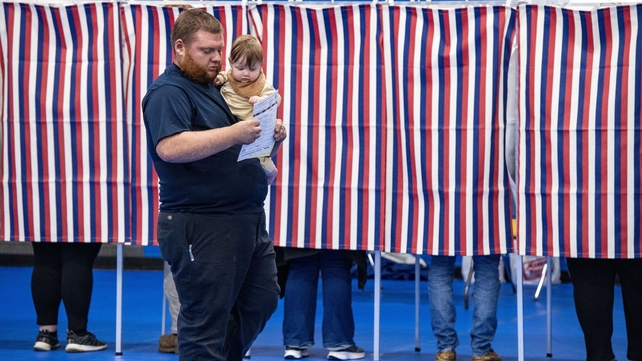 A man carries a baby with a filled out ballot after voting at the Green Street Community Centre in Concord, New Hampshire