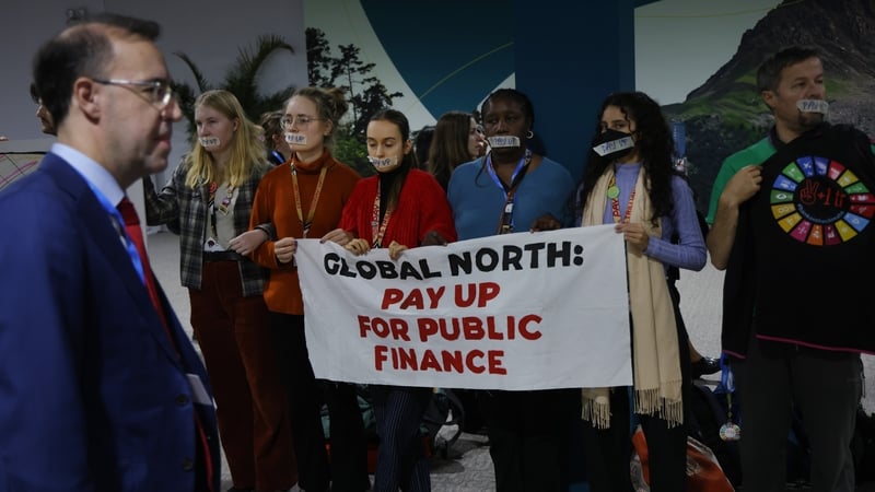 Conference participants walk past activists urging public climate finance for developing nations impacted by climate change