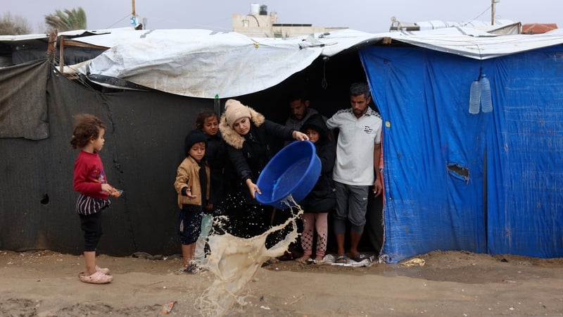 A displaced Palestinian woman tries to remove rainwater from her tent following heavy rainfall in Gaza