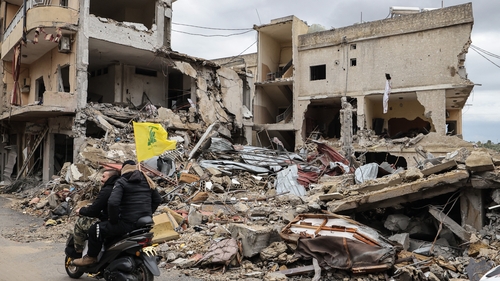 Men ride a scooter with a Hezbollah flag past destroyed buildings as people make their way back to their homes in south Lebanon
