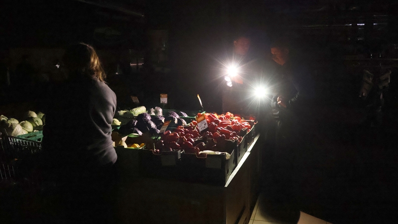 Customers use their phones to illuminate vegetables in a supermarket during a power outage in Kyiv, Ukraine
