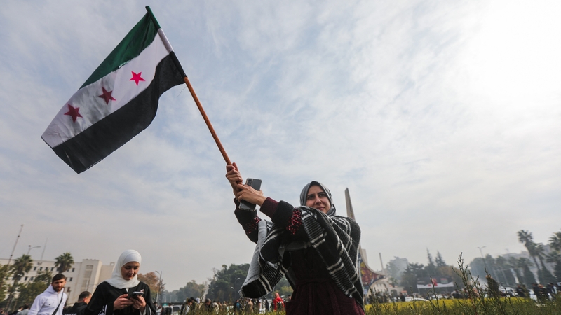 A woman waves a Syrian opposition flag as she celebrates at Umayyad Square in Damascus